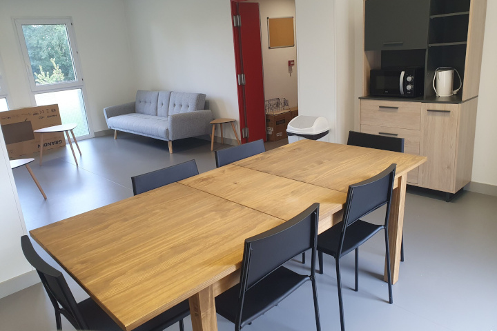 Espace de vie commun meublé avec table en bois, chaises noires, canapé et coin cuisine de la résidence étudiante du Campus Saint Aubin La Salle